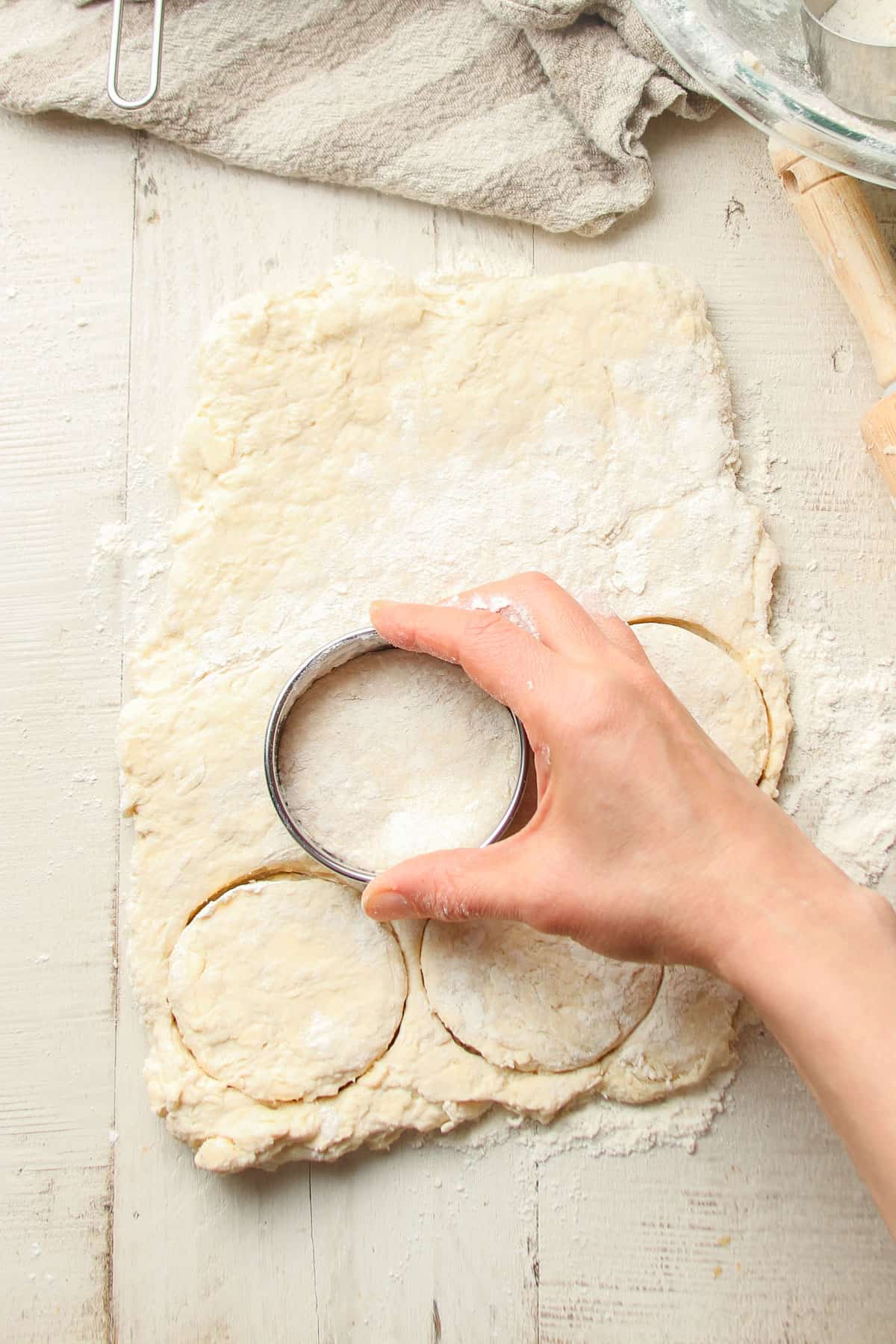Hand cutting biscuits in dough using a biscuit cutter.