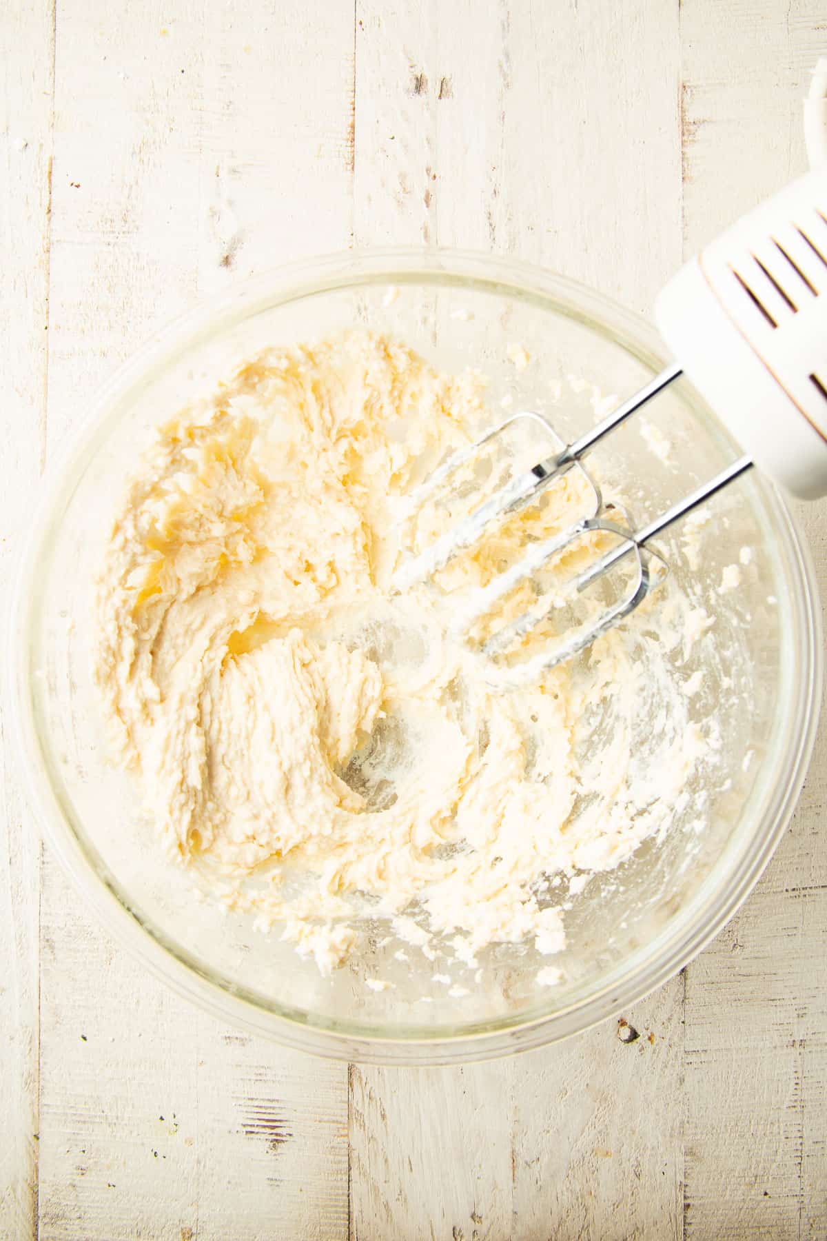 Creamed mixture of vegan butter, cream cheese, and vanilla extract in a mixing bowl with electric mixer.