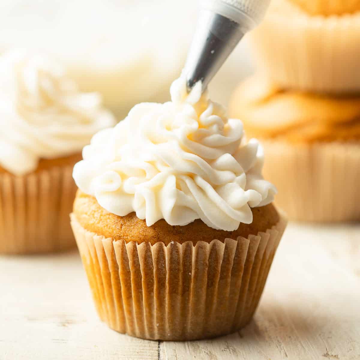 Vegan Cream Cheese Frosting being piped onto a pumpkin cupcake.