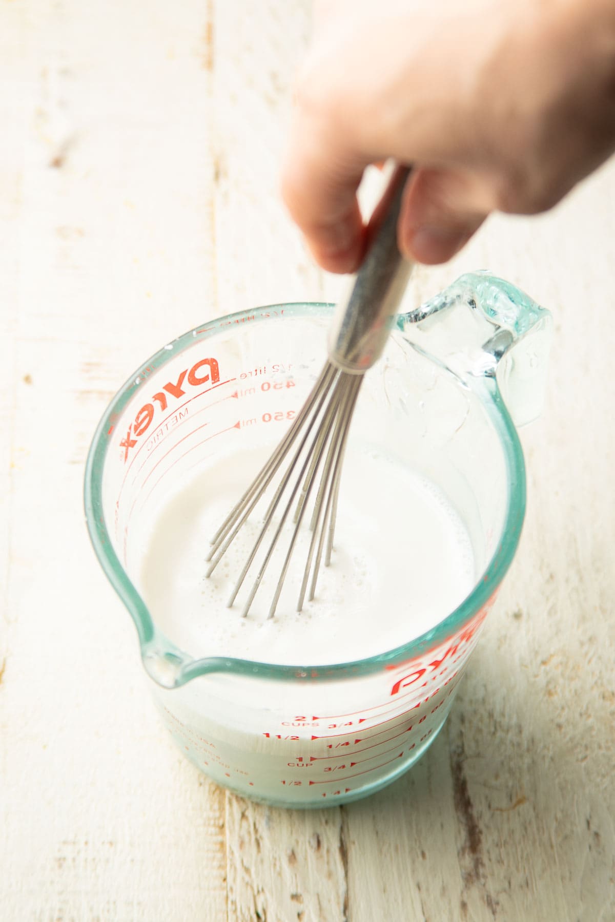 Hand whisking cornstarch and non-dairy milk together in a measuring cup.