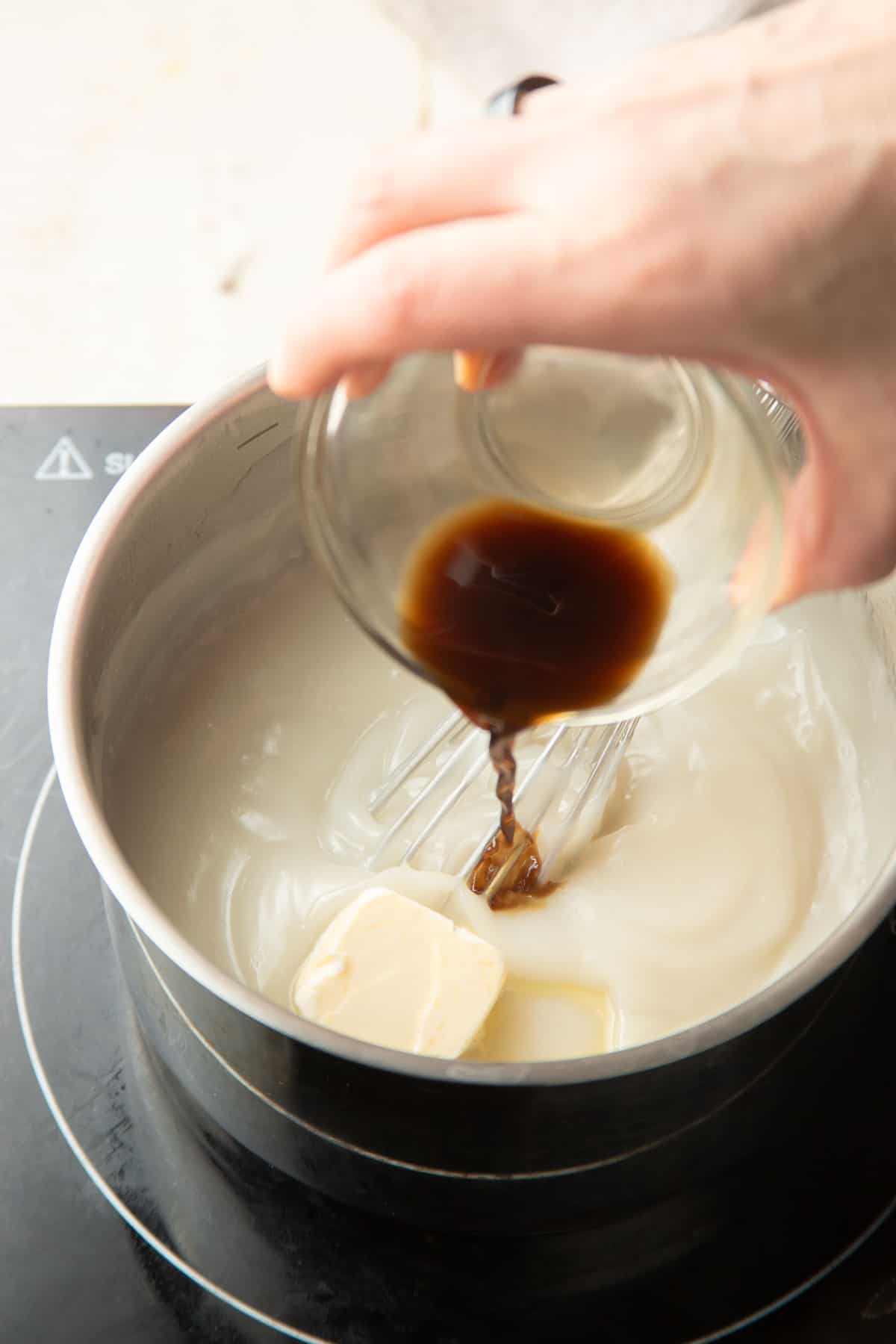 Hand pouring vanilla into a pot of Vegan Custard with a slice of vegan butter on top.