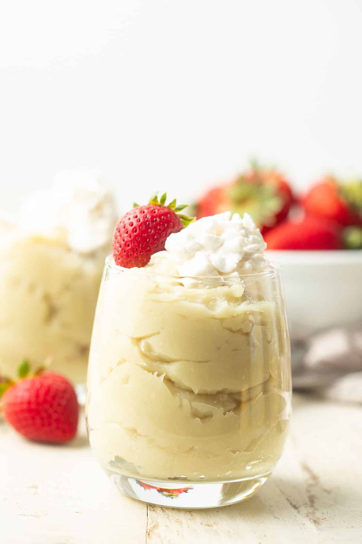 Jar of Vegan Custard with a bowl of strawberries in the background.