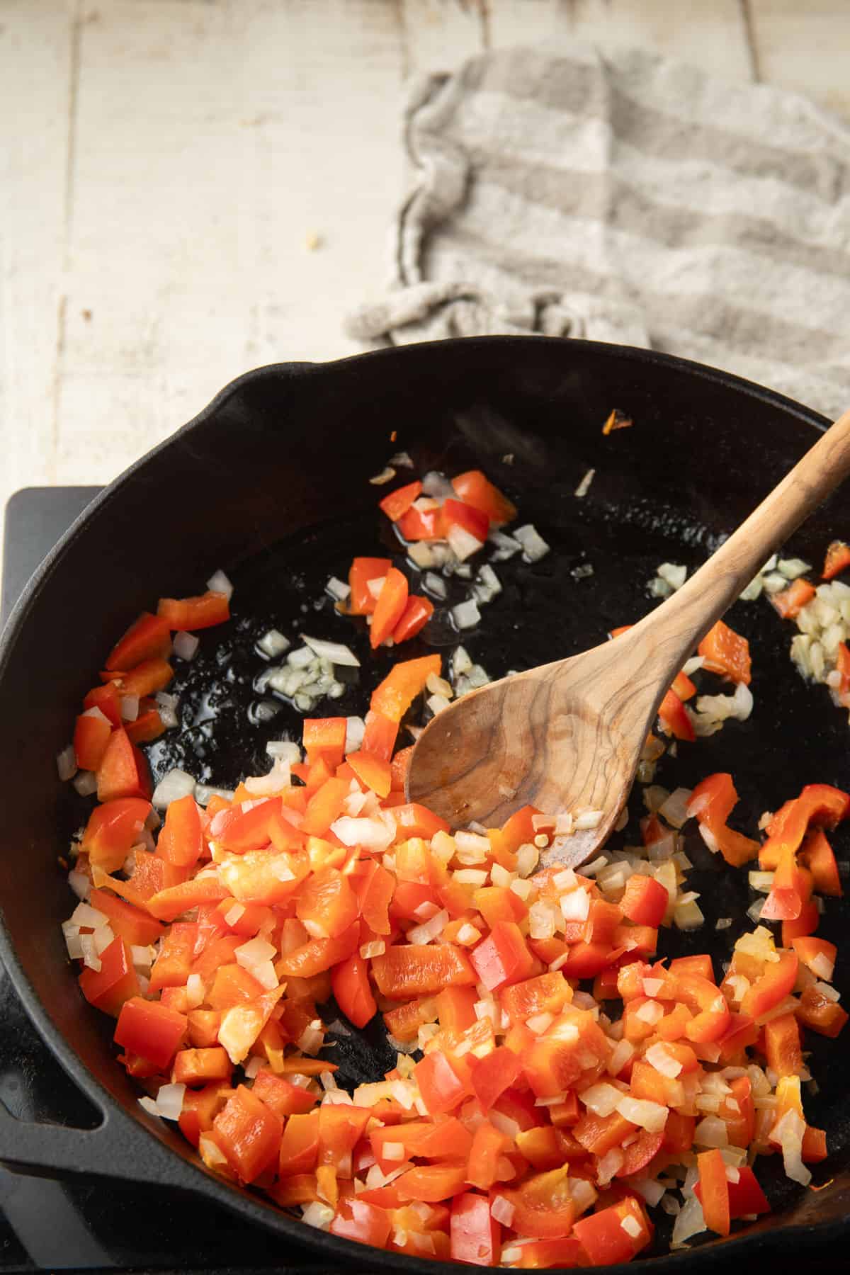 Red bell pepper and onion cooking in oil in a skillet.