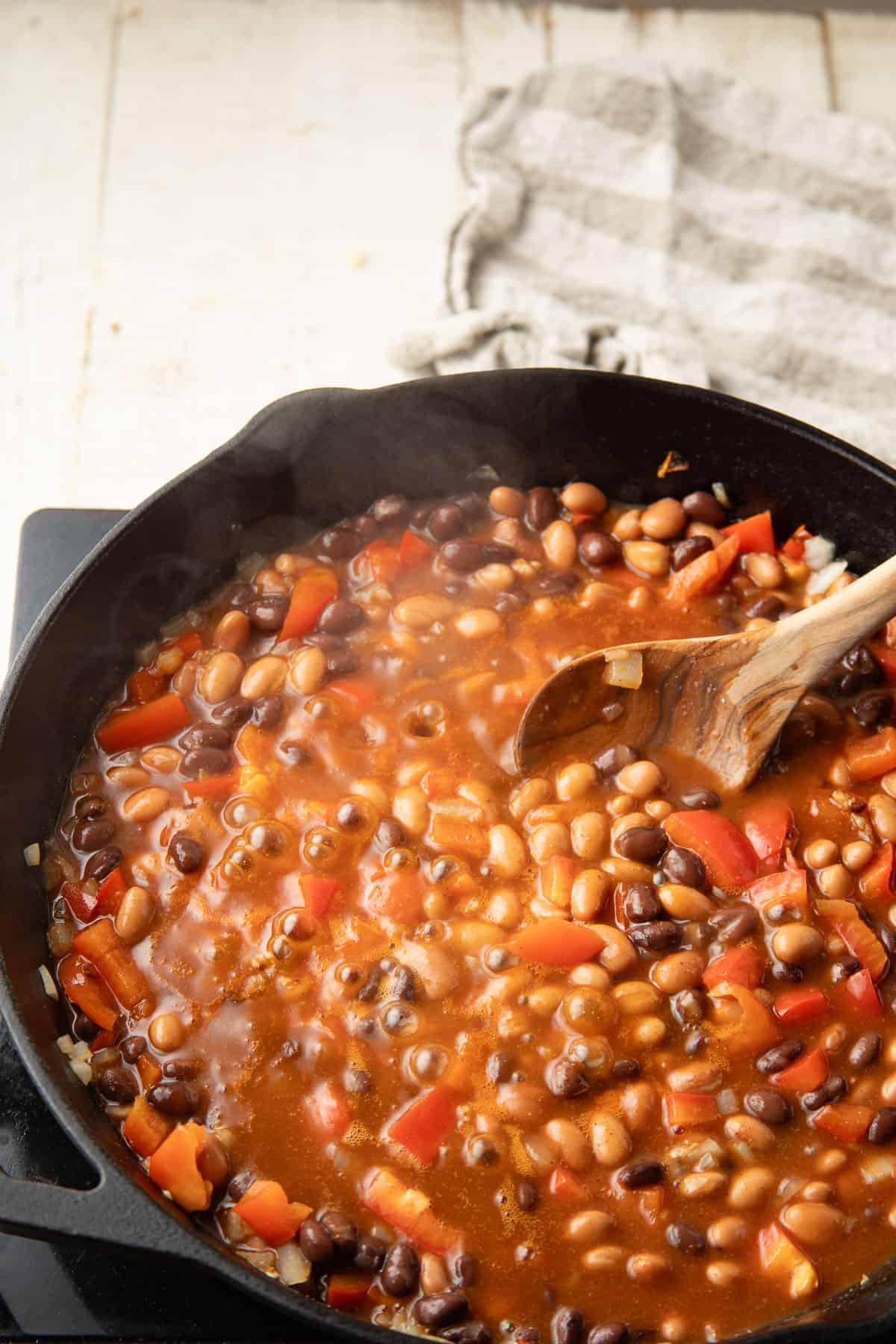 Beans simmering in enchilada sauce in a skillet.
