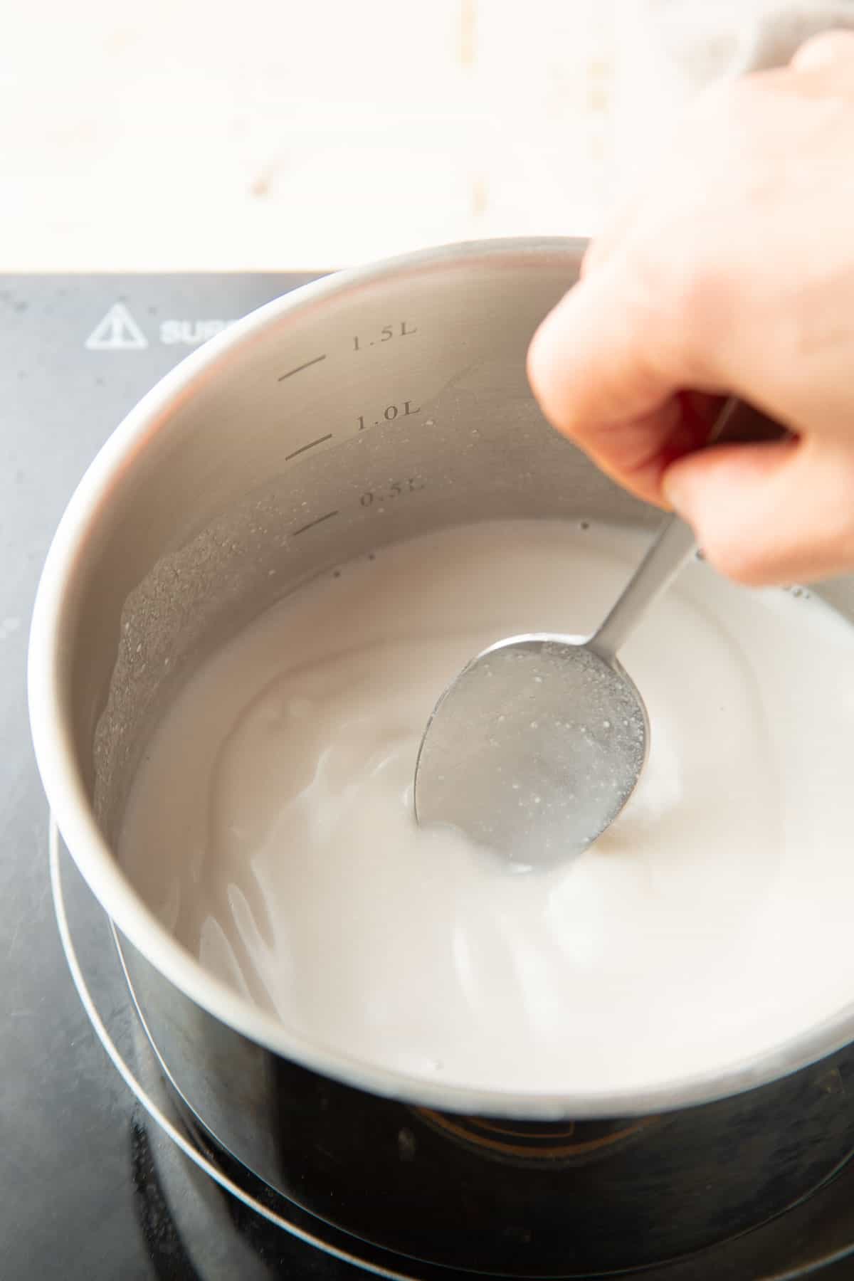 Hand stirring coconut milk in a saucepan.