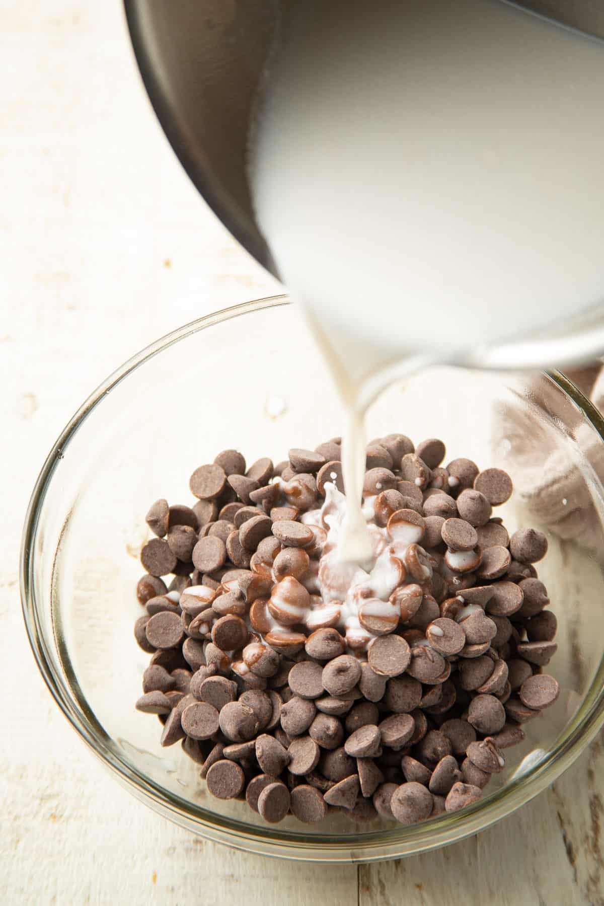 Hot coconut milk being poured over a bowl of chocolate chips.