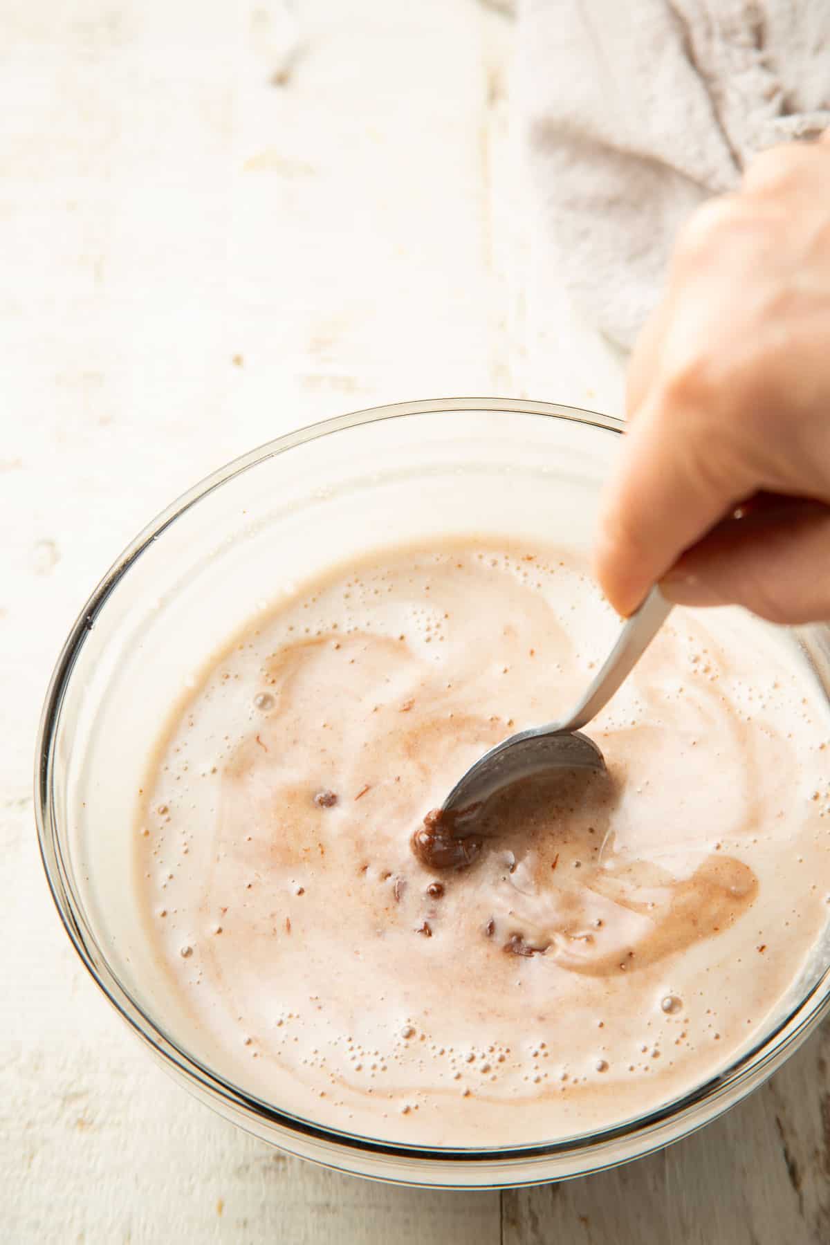 Hand stirring coconut milk and chocolate together in a bowl.