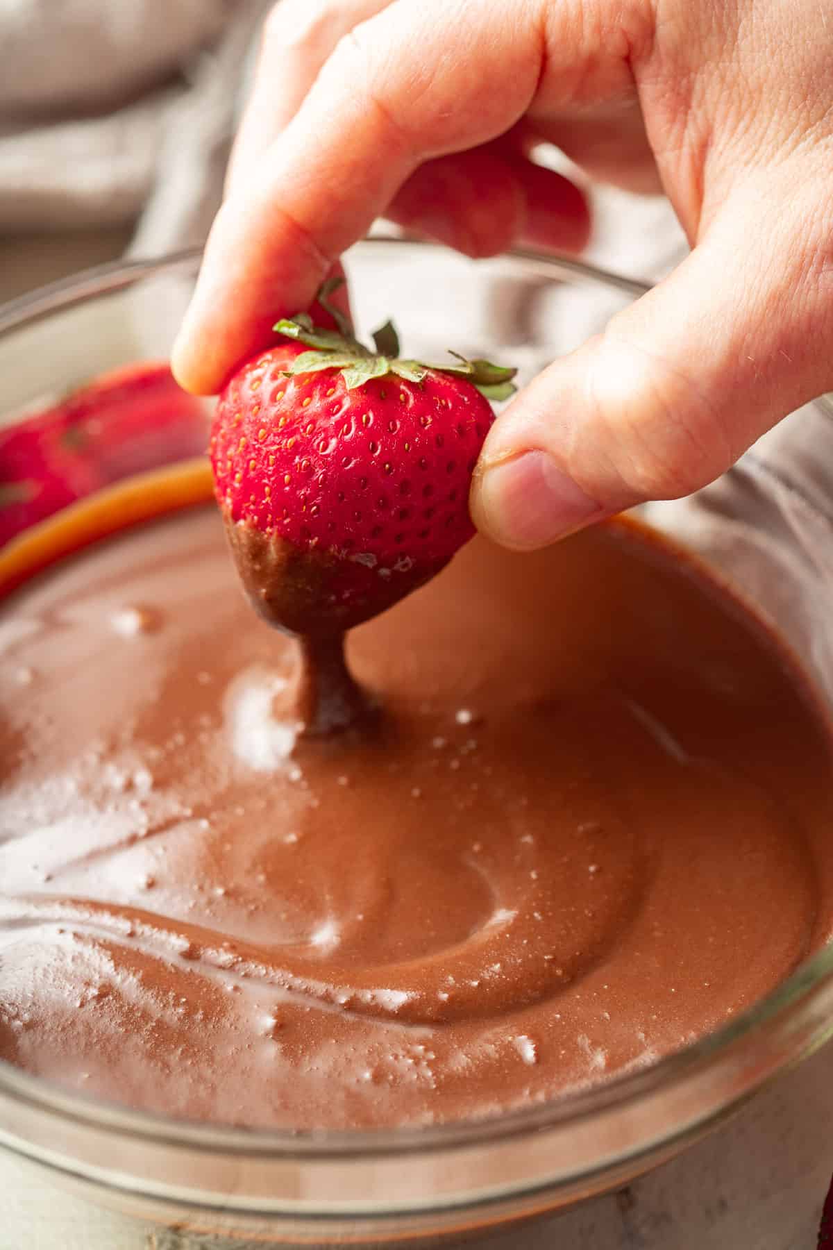 Hand dipping a strawberry into a bowl of Vegan Ganache.