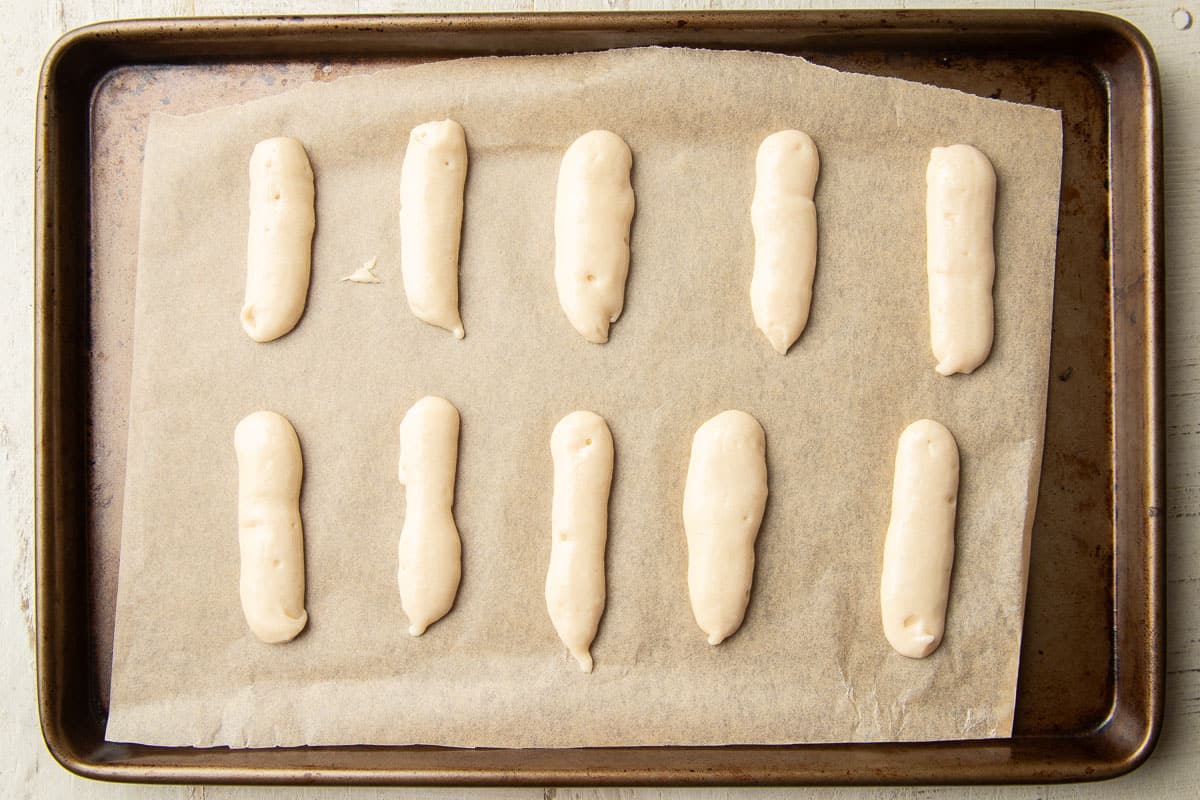 Unbaked Vegan Ladyfingers on a parchment paper-lined baking sheet.