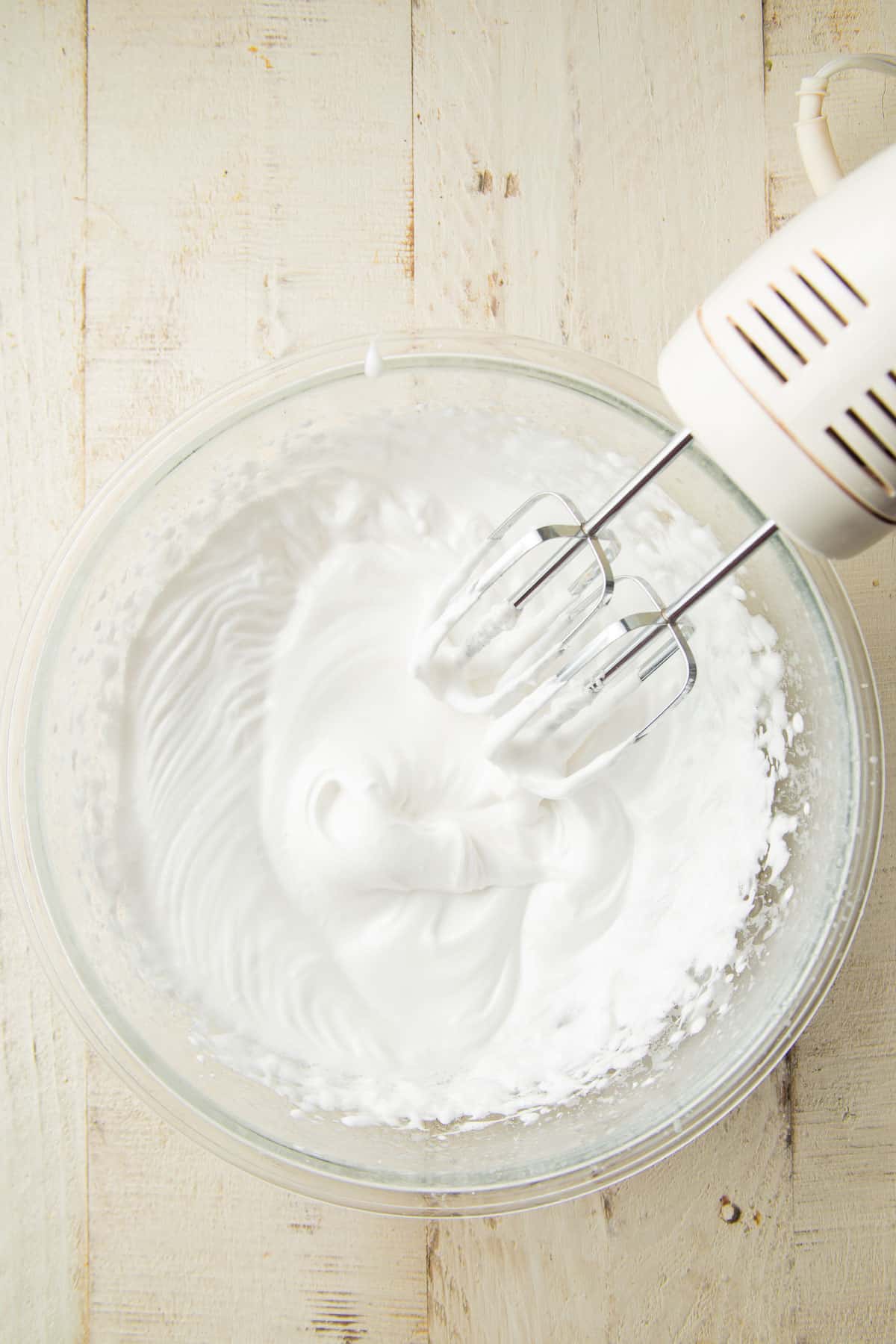 Whipped aquafaba in a mixing bowl with electric mixer.