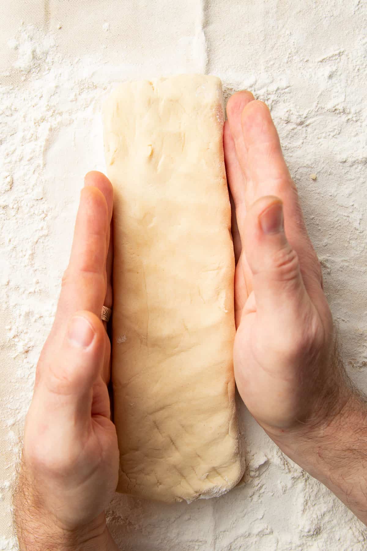 Hands shaping vegan shortbread dough into a rectangle.