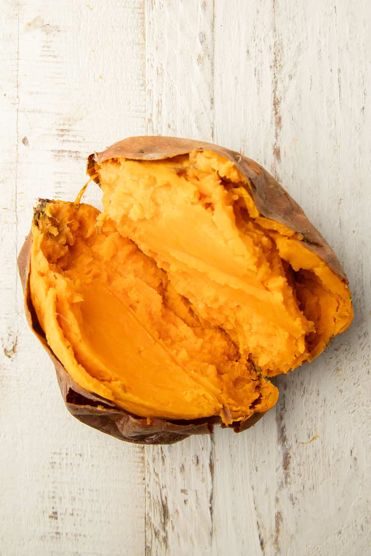 Baked sweet potato that's been cut open on a white wooden surface.