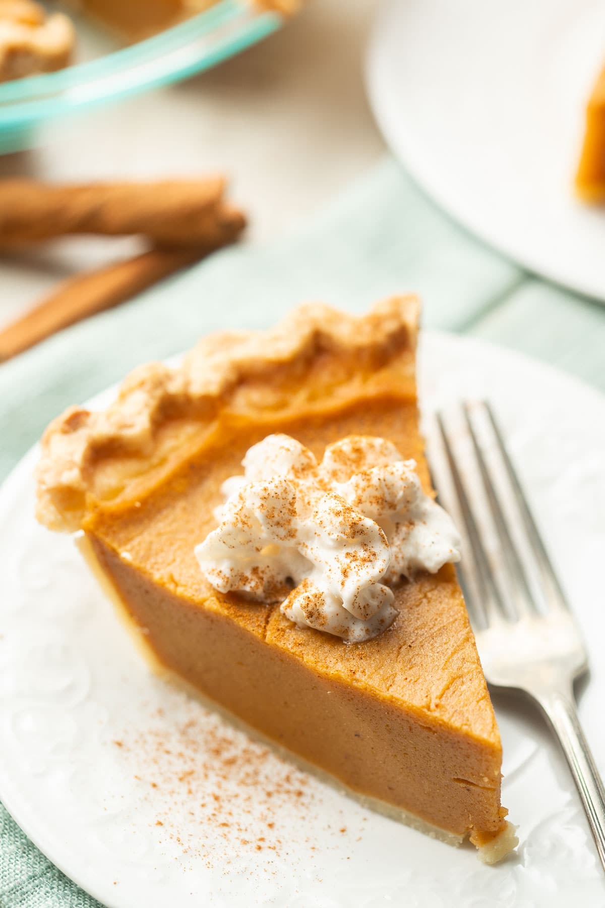 Slice of Vegan Sweet Potato Pie topped with whipped cream and cinnamon on a dish.