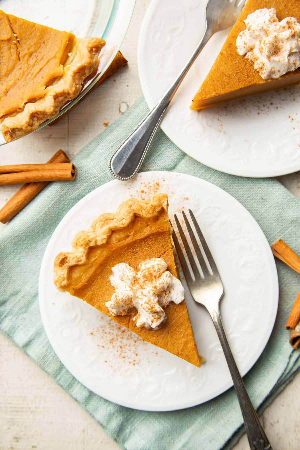 Surface set with two slices of Vegan Sweet Potato Pie on dishes, and a pie plate.
