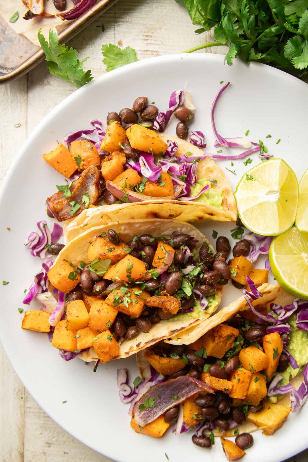 Dish of Butternut Squash Tacos and lime slices on a white wooden surface.