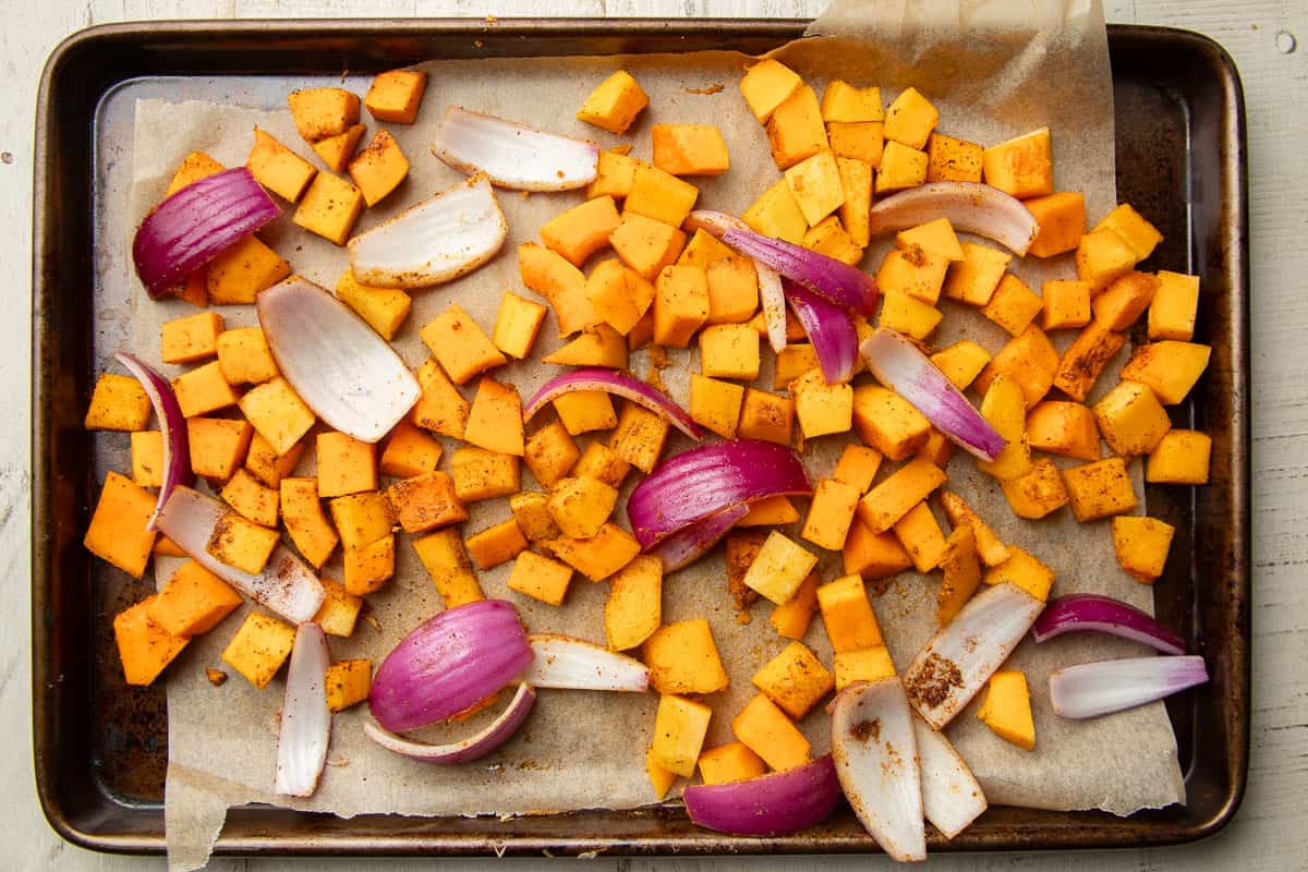 Diced butternut squash and sliced red onion on a baking sheet.