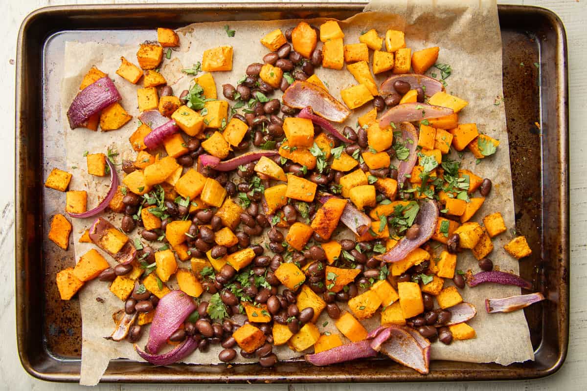Roasted butternut squash, onions, and black beans on a baking sheet with chopped fresh cilantro.