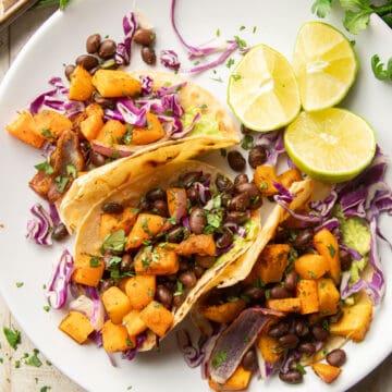 Three Butternut Squash Tacos on a dish with lime slices.
