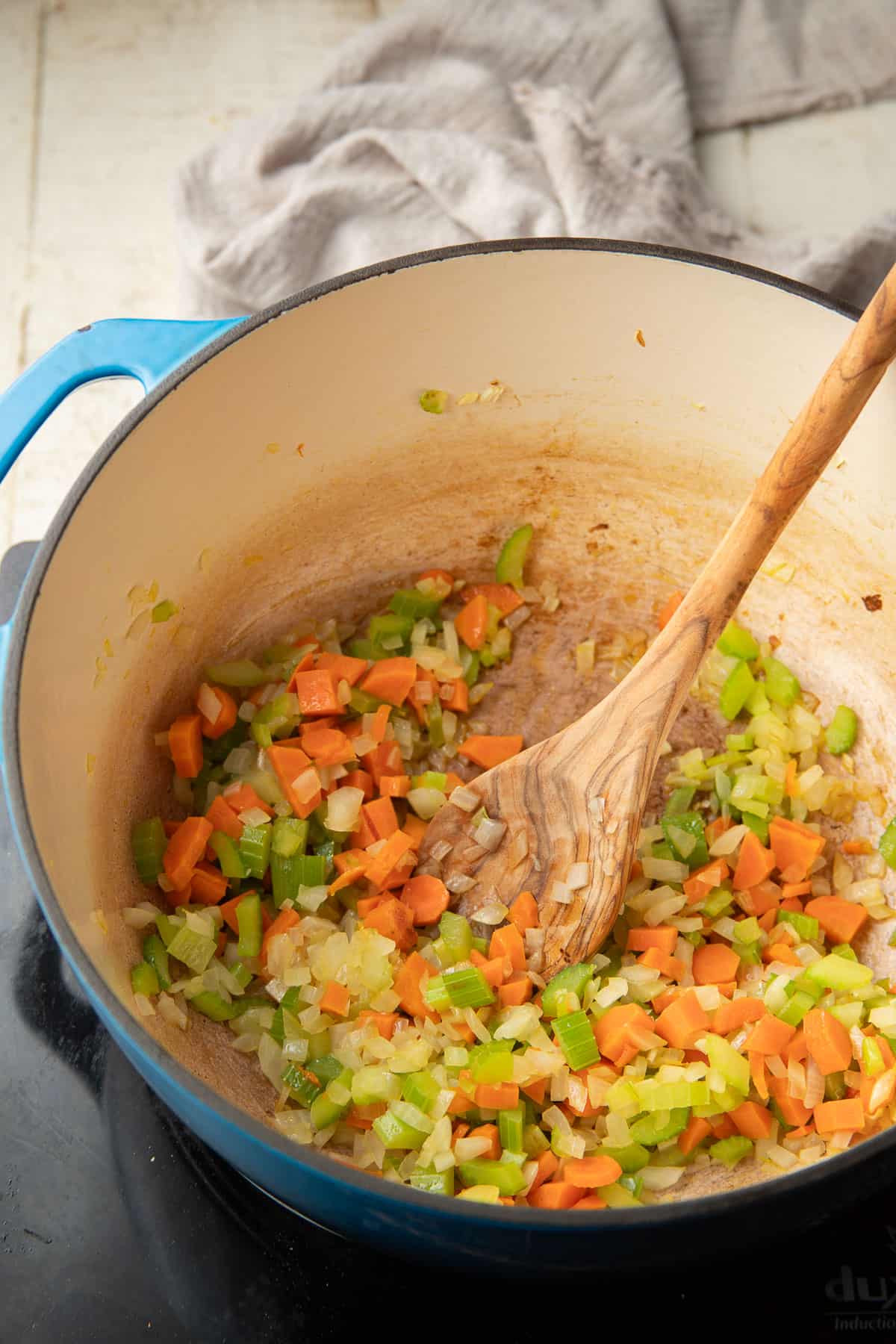 Carrots, celery, garlic, and onion cooking in a pot with wooden spoon.