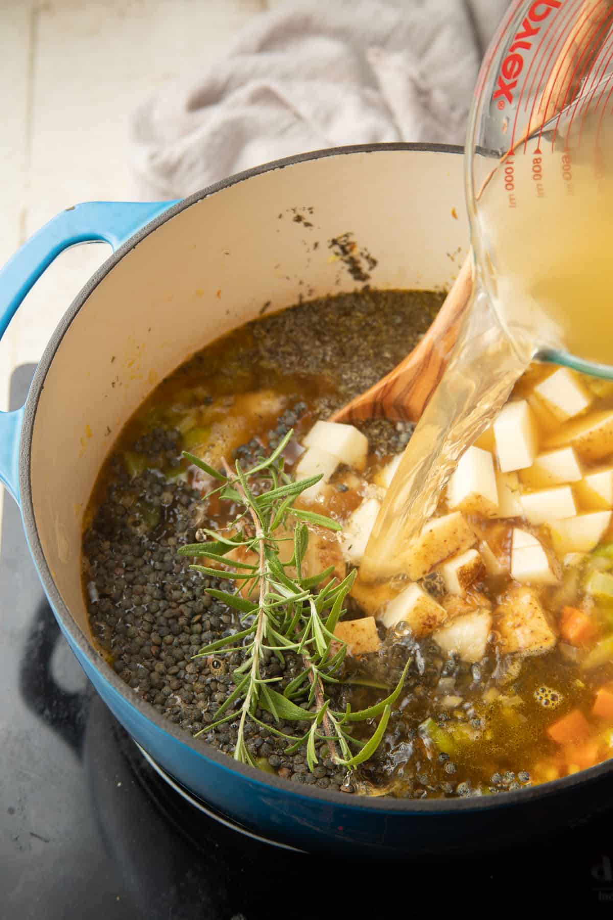 Broth being poured into a pot of French lentils, potatoes, vegetables and herbs.