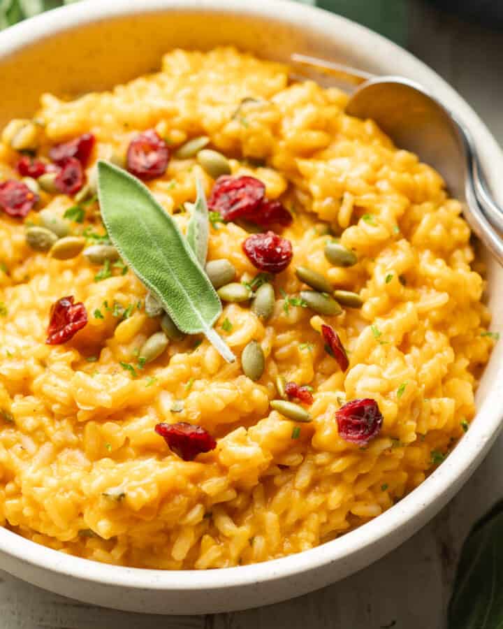 Bowl of Pumpkin Risotto topped with pumpkin seeds, cranberries and fresh sage.