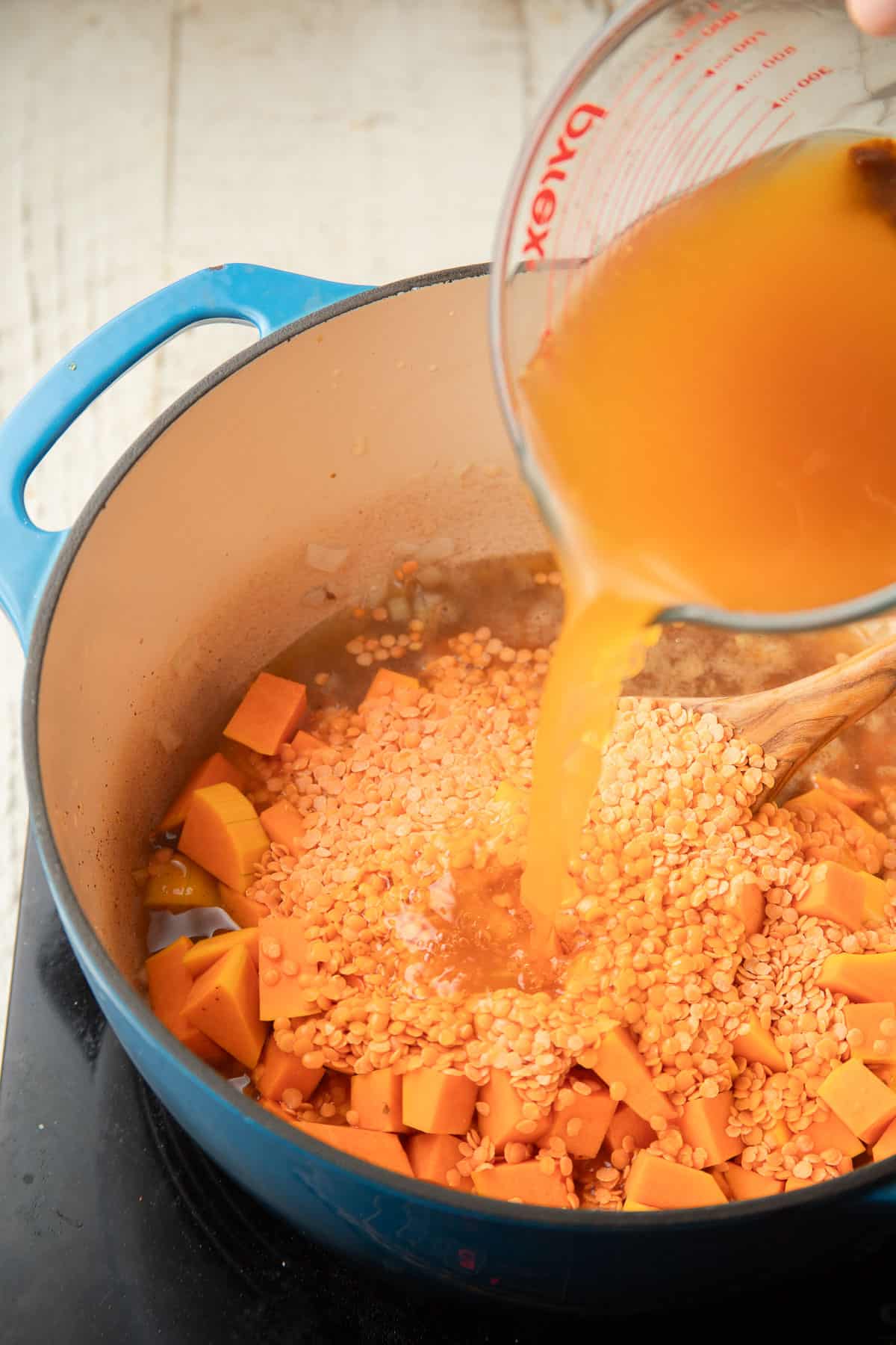 Broth being poured into a pot filled with red lentils and butternut squash.