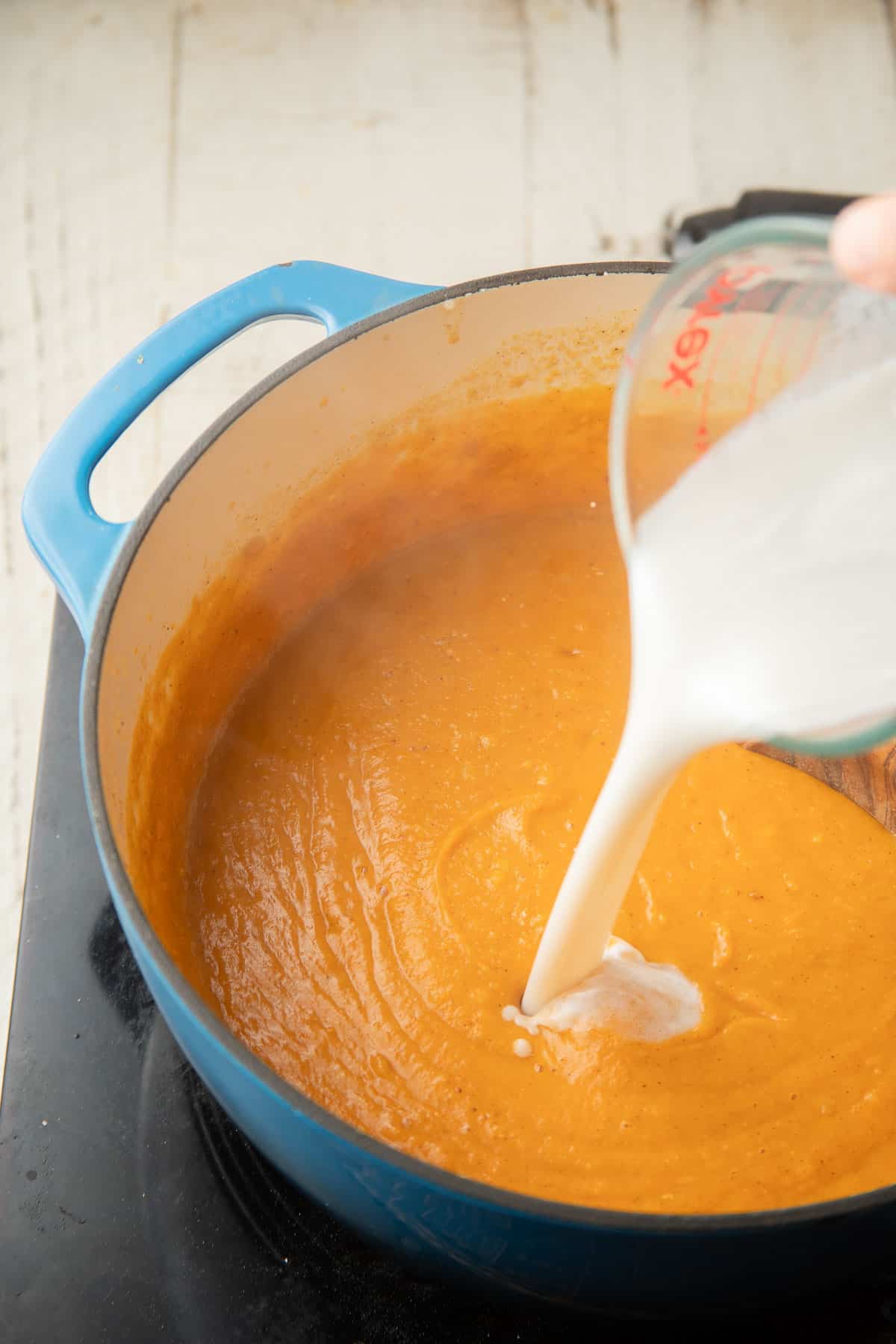 Coconut milk being poured into a pot of Red Lentil Butternut Squash Soup.