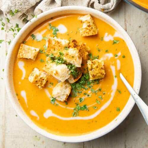 Bowl of Red Lentil Butternut Squash Soup topped with croutons, fresh cilantro, and coconut milk drizzle.