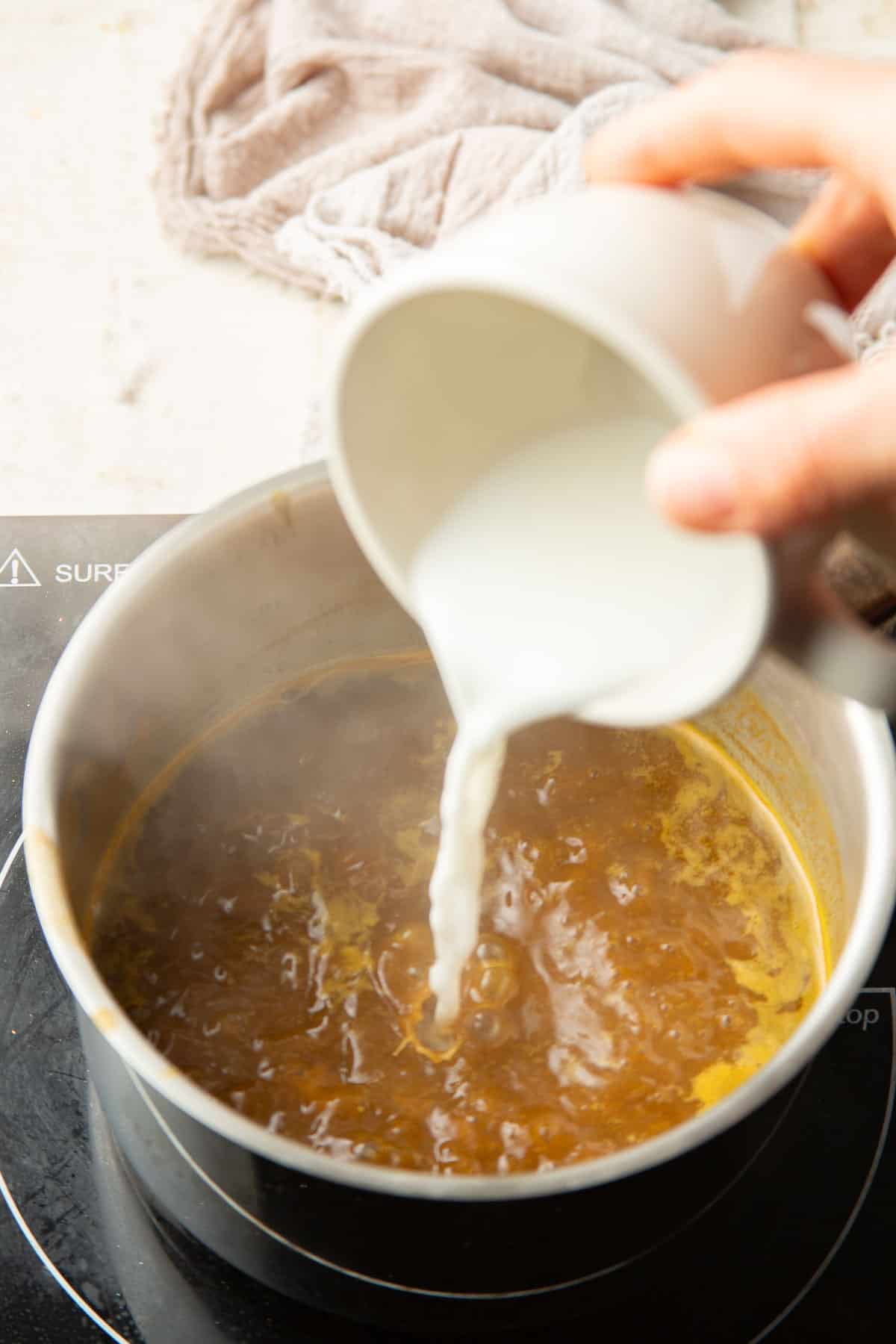 Hand pouring cornstarch slurry into a saucepan of curry sauce.