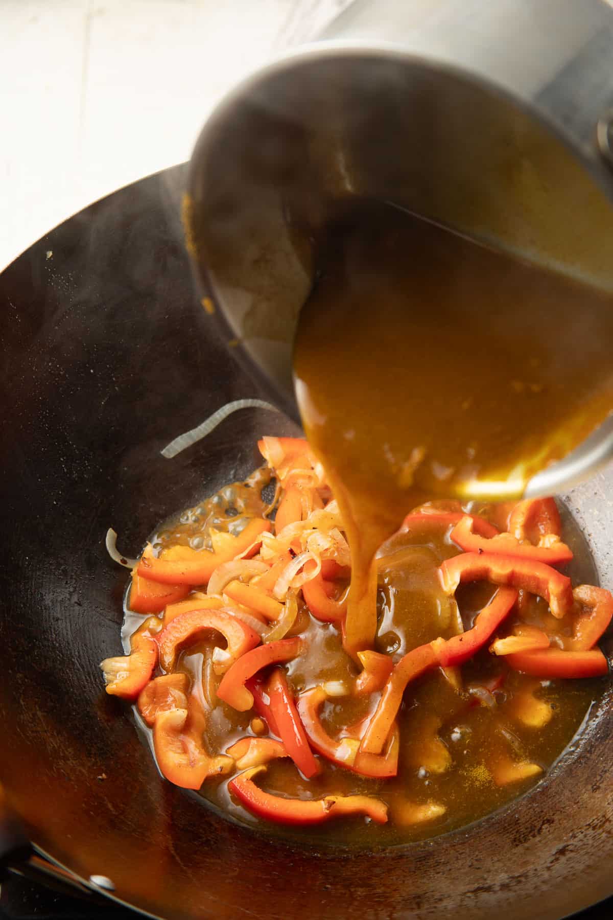 Vegan Chinese Curry sauce being poured over peppers and onions in a wok.