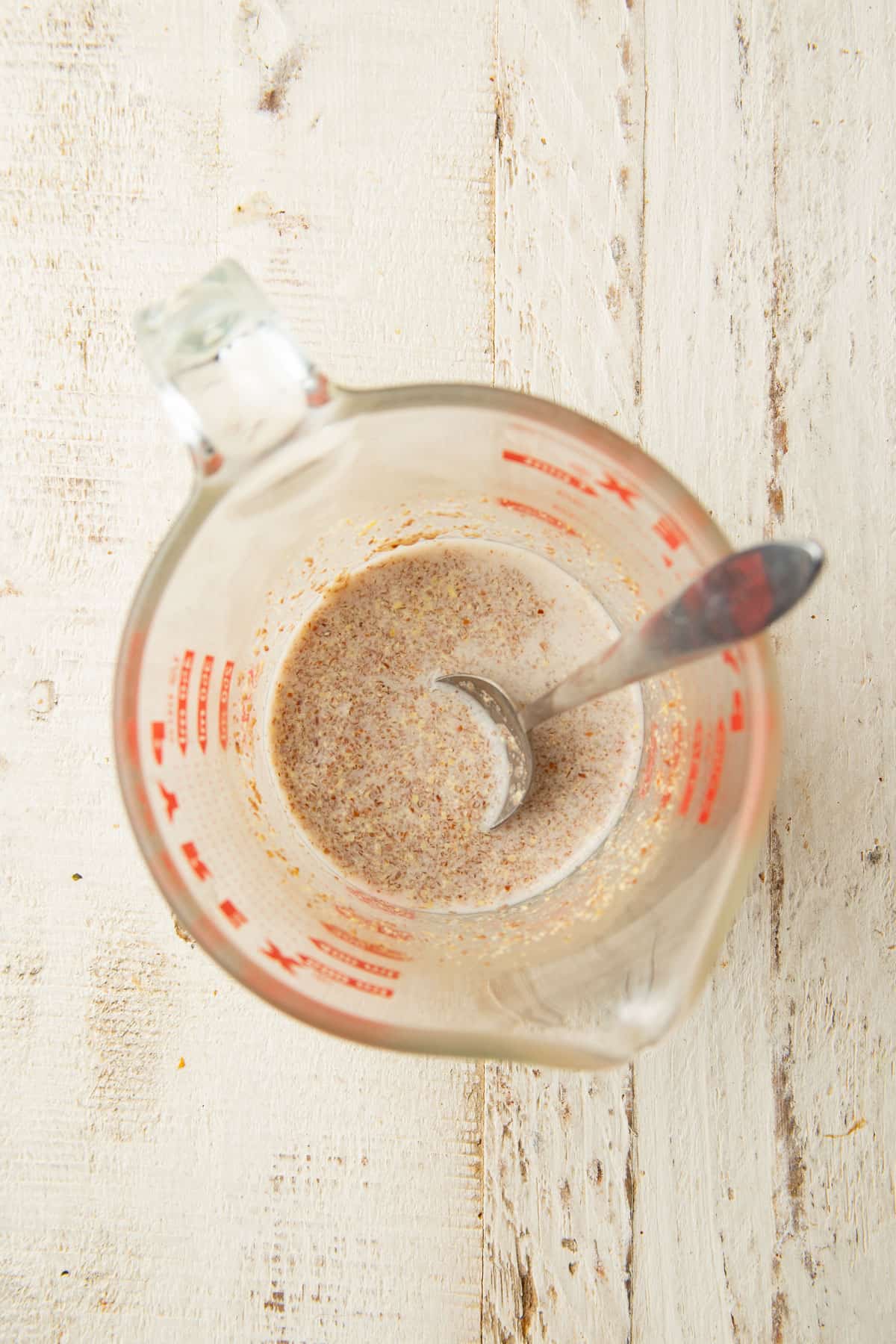 Mixture of ground flaxseeds and non-dairy milk in a liquid measuring cup with a spoon.