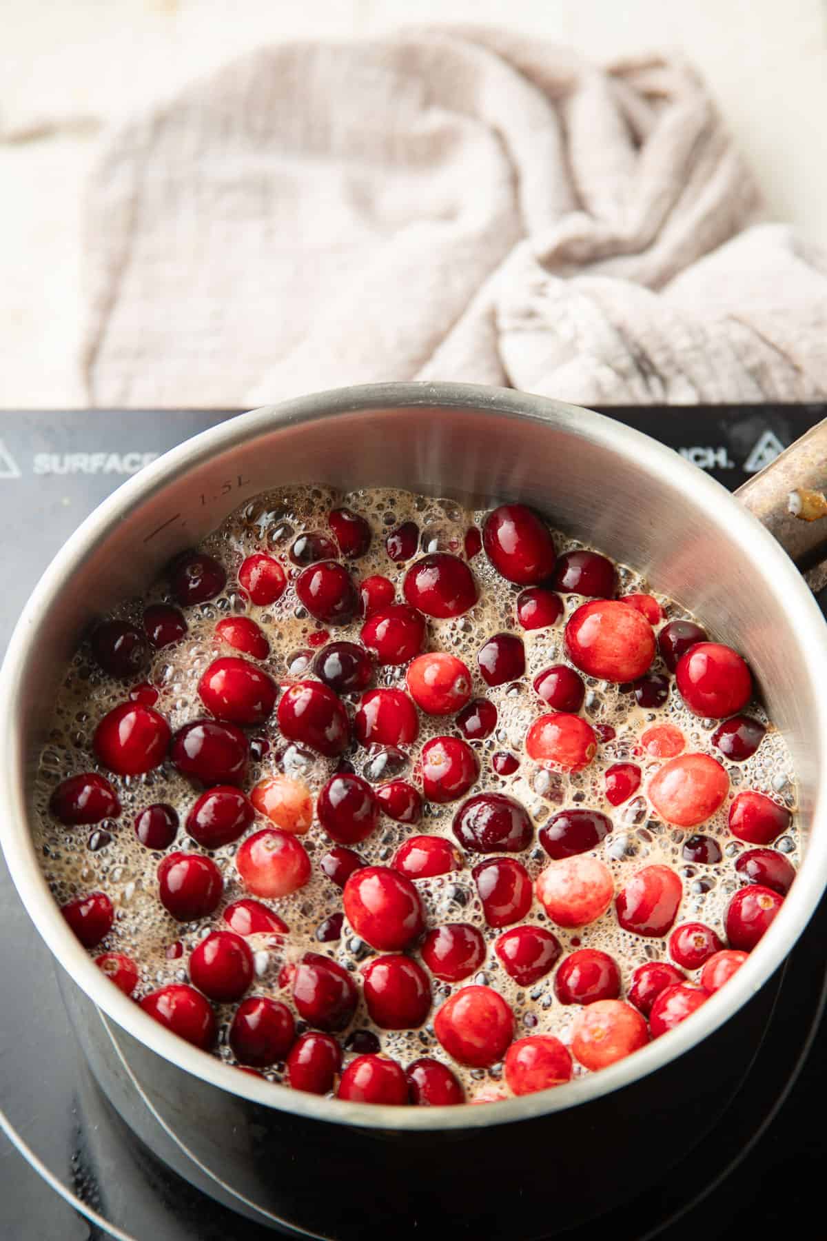Cranberries in simmering liquid in a saucepan.