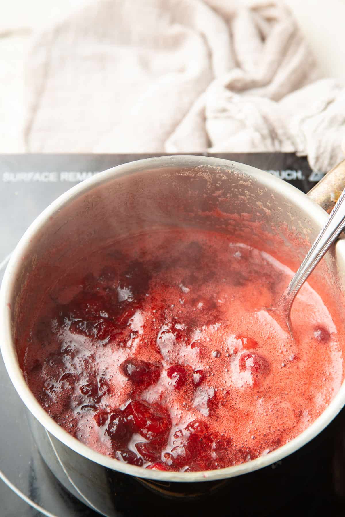 Vegan Cranberry Sauce simmering in a saucepan with spoon.