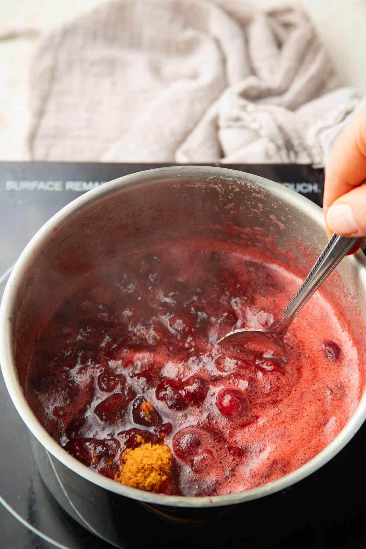 Orange zest being stirred into a pot of Vegan Cranberry Sauce.