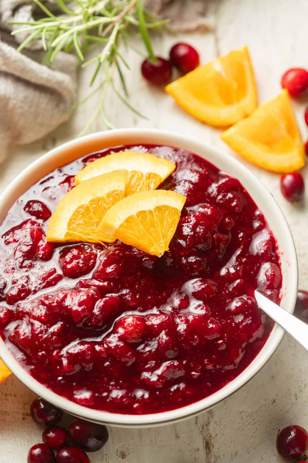Bowl of Vegan Cranberry Sauce with orange slices, cranberries and fresh rosemary in the background.