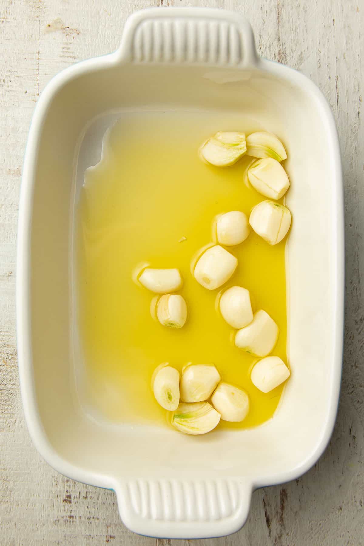 Raw garlic cloves and olive oil in a baking dish.
