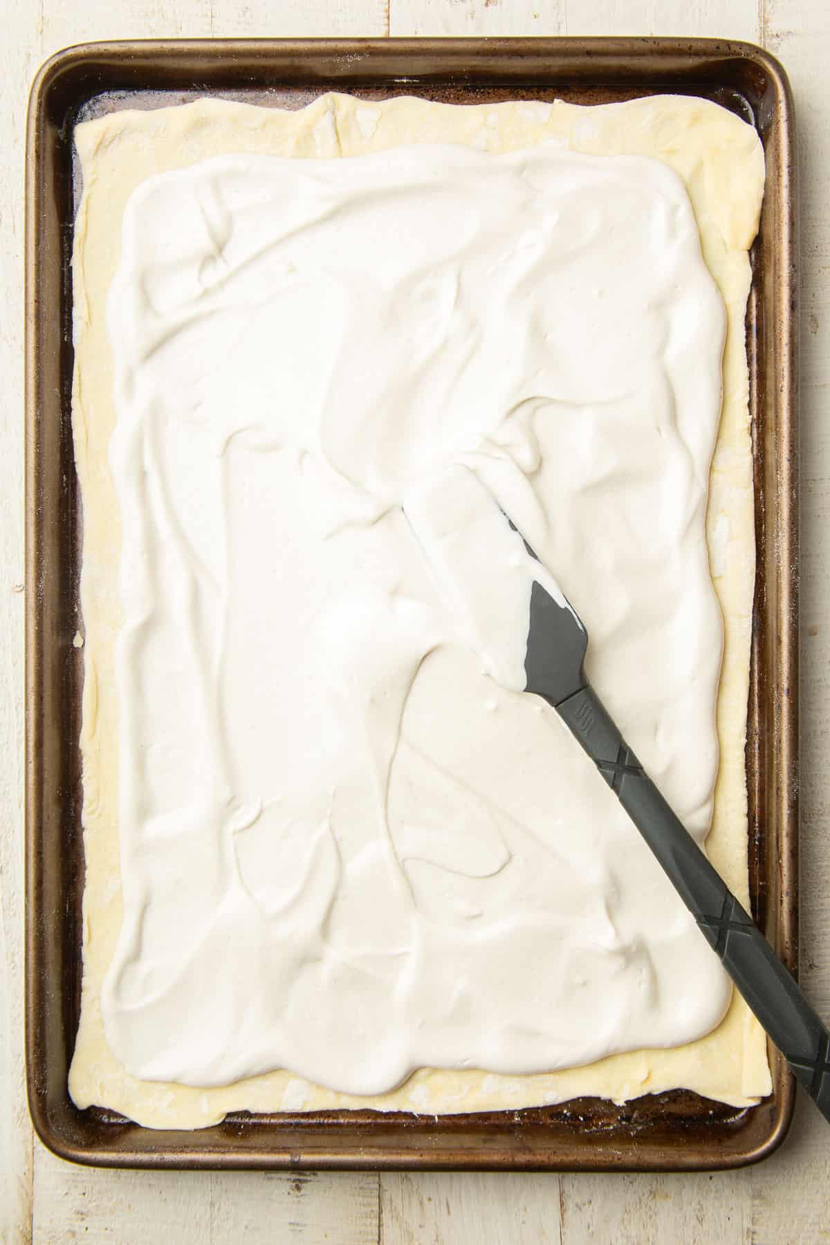 Cashew cheese being spread over a sheet of puff pastry on a baking sheet.