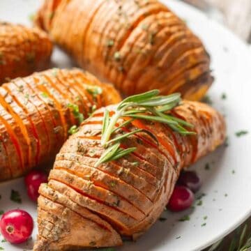 Hasselback Sweet Potatoes on a plate with fresh rosemary and cranberries.
