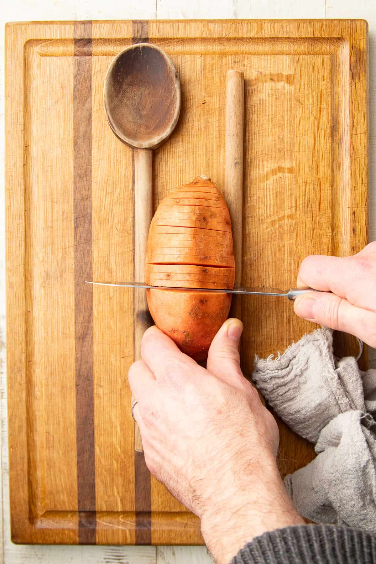 Hands slicing a hasselback arrangement into a sweet potato.