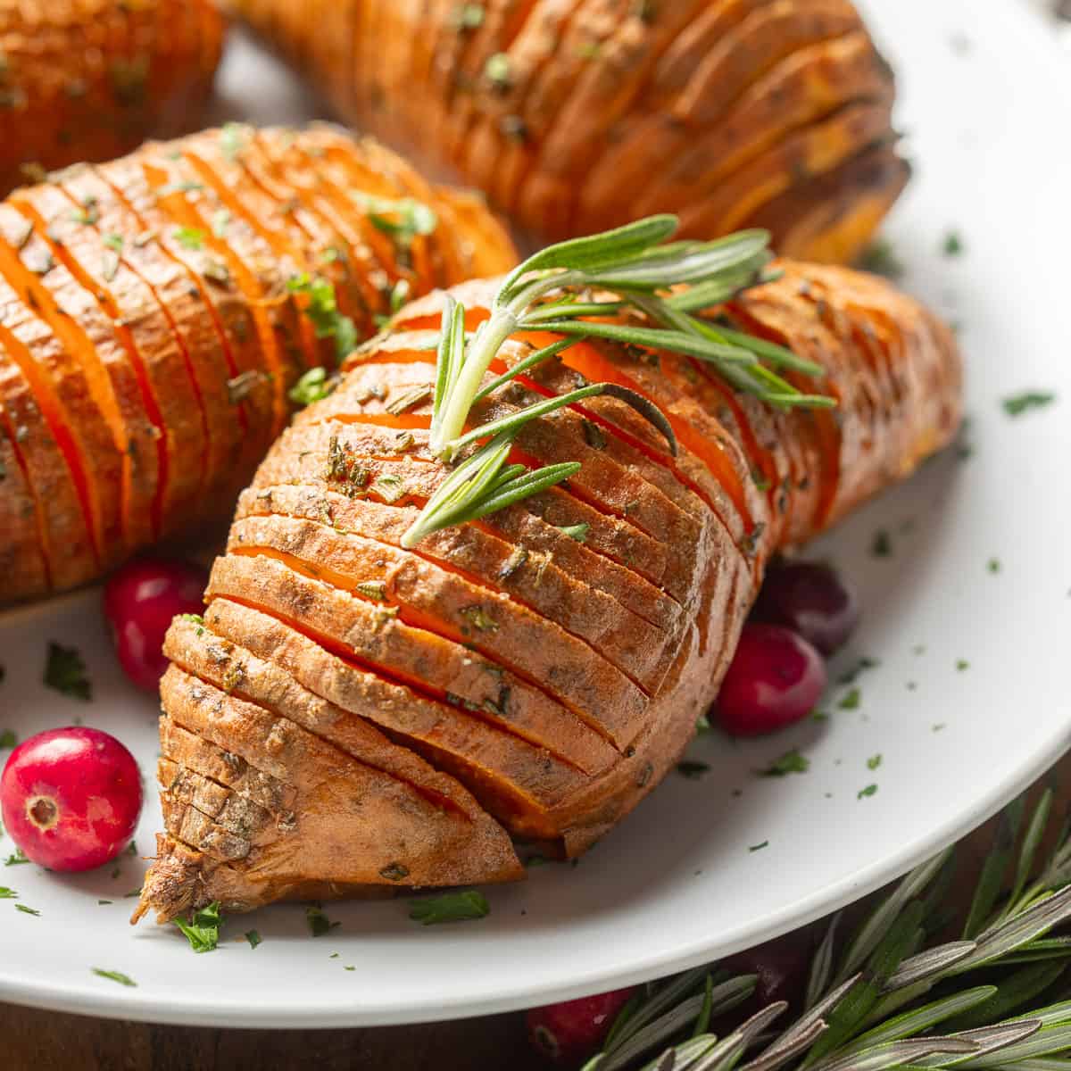 Hasselback Sweet Potatoes on a plate with fresh rosemary and cranberries.