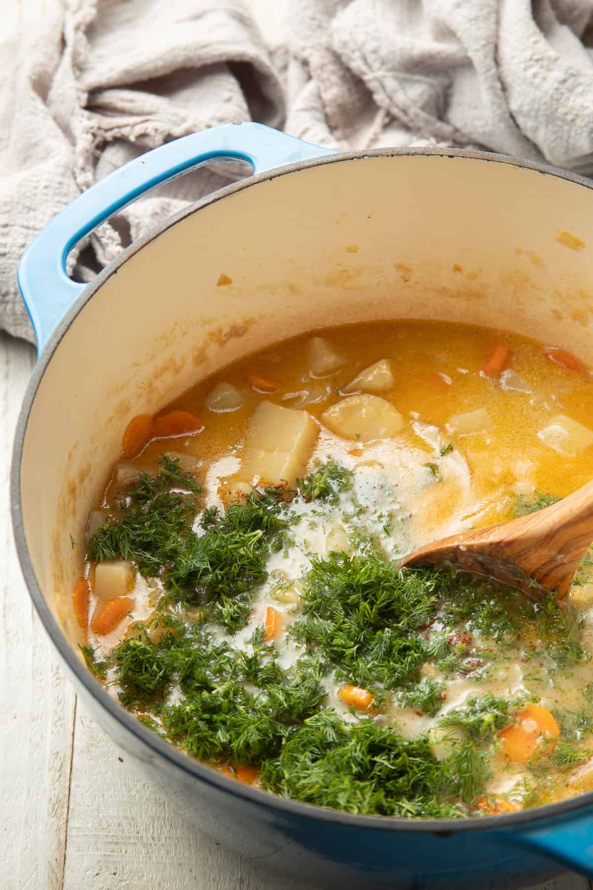 Spoon stirring chopped dill into a pot of potato soup.