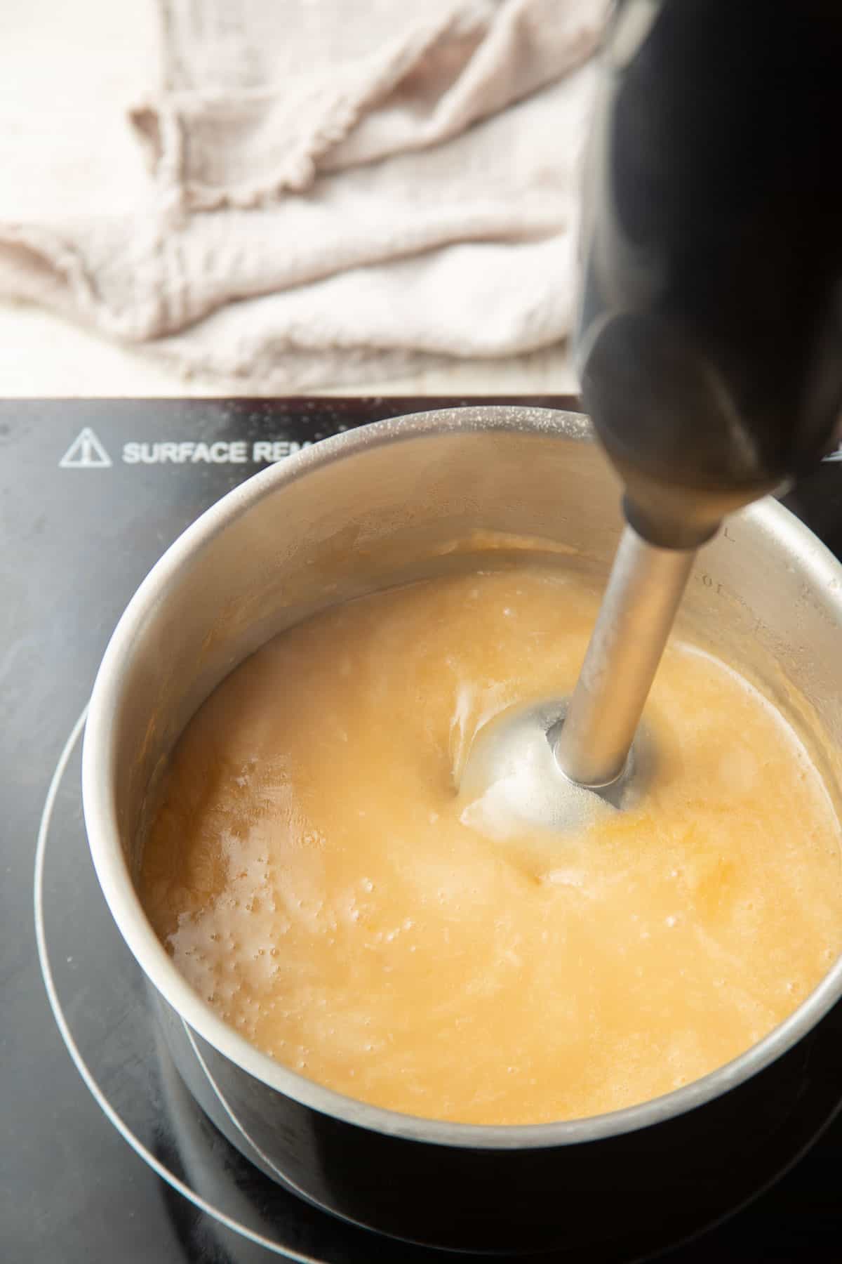Immersion blender blending gravy in a saucepan.