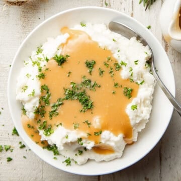 Bowl of mashed potatoes topped with Roasted Garlic Gravy and fresh parsley.