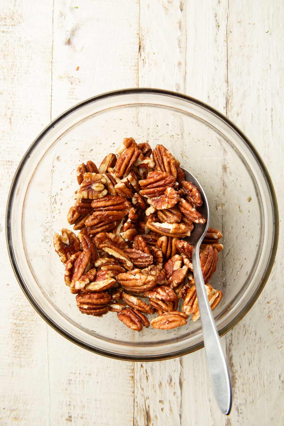 Bowl of pecans covered in maple syrup with a spoon.