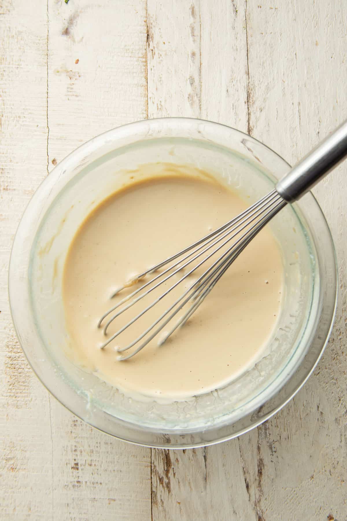 Tahini dressing in a bowl with wire whisk.