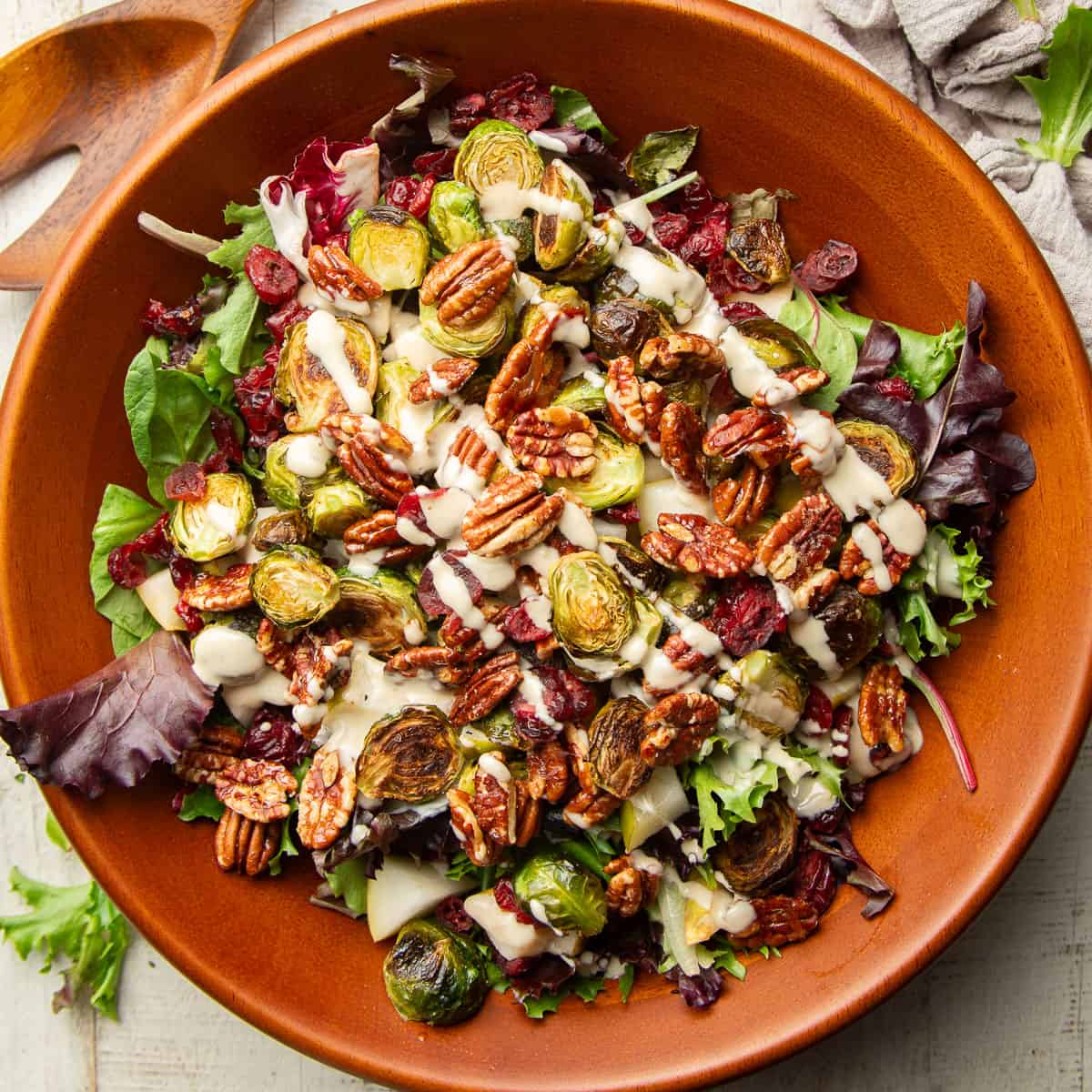 Wooden bowl of salad with pecans, brussels sprouts, dried cranberries and diced pears.