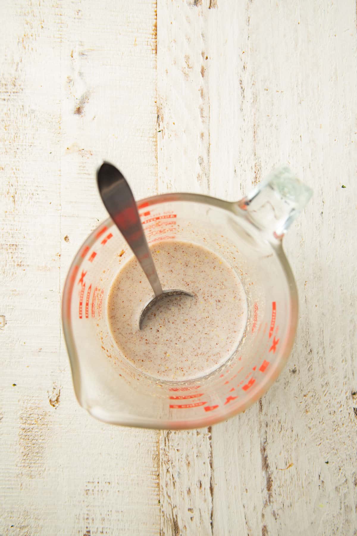 Non dairy milk and ground flaxseed in a liquid measuring cup with spoon.