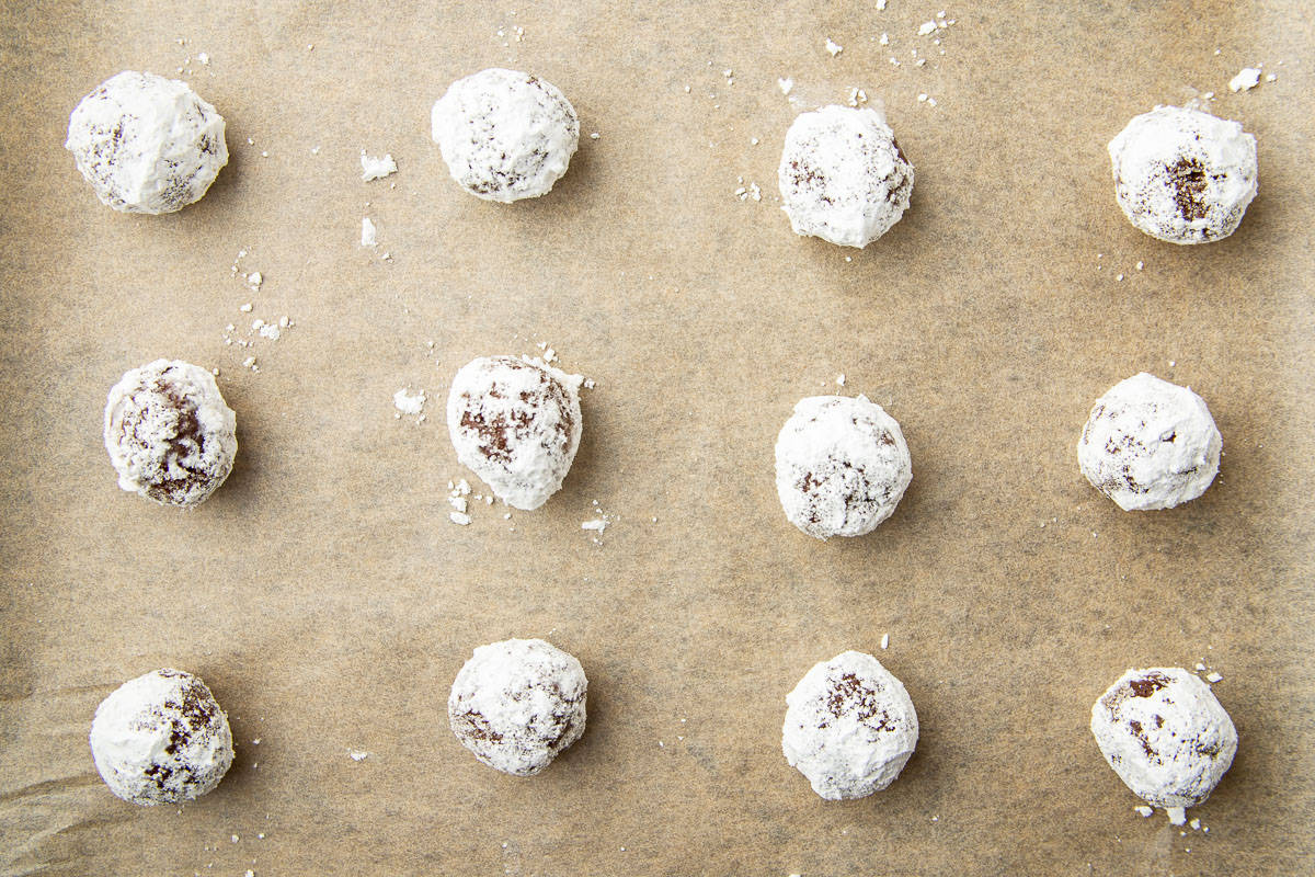 Chocolate cookie dough balls coated in powdered sugar on a parchment paper lined baking sheet.