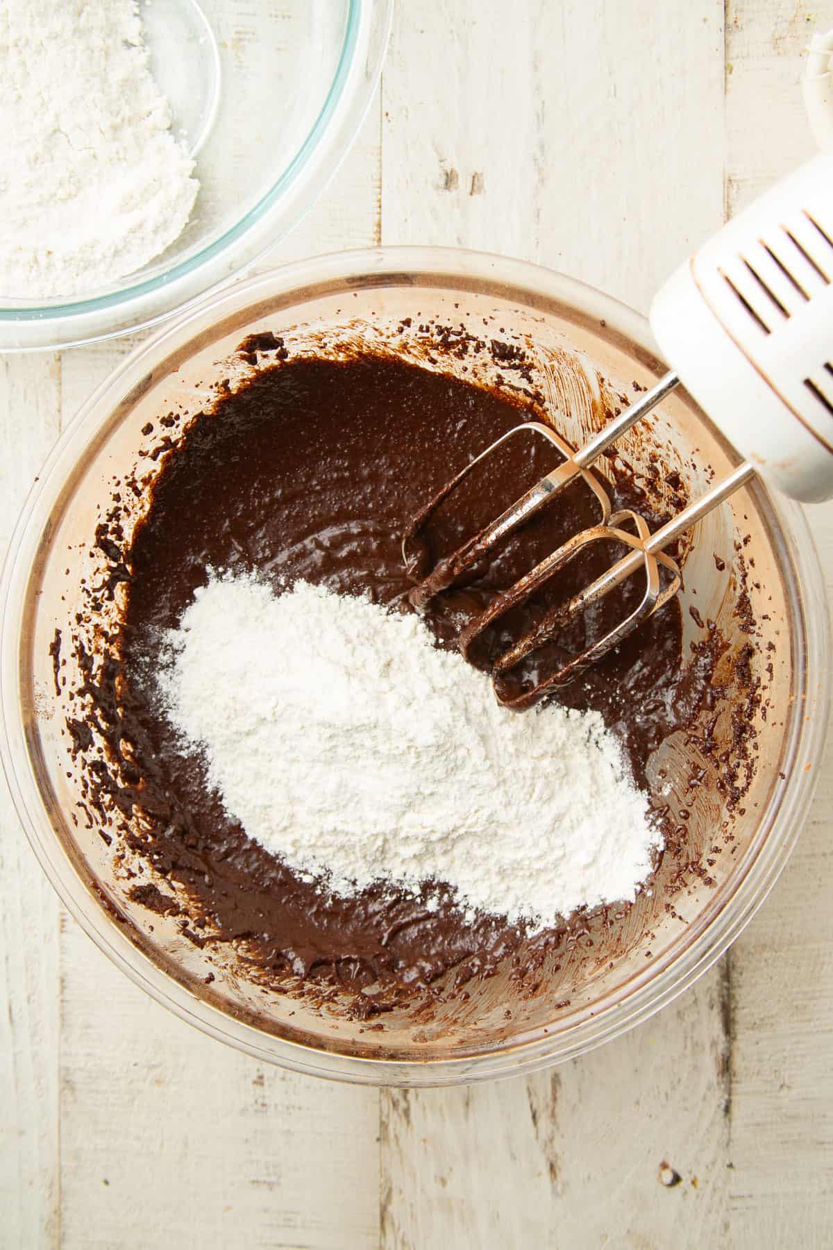 Flour being added to chocolate cookie dough in a bowl with mixer.