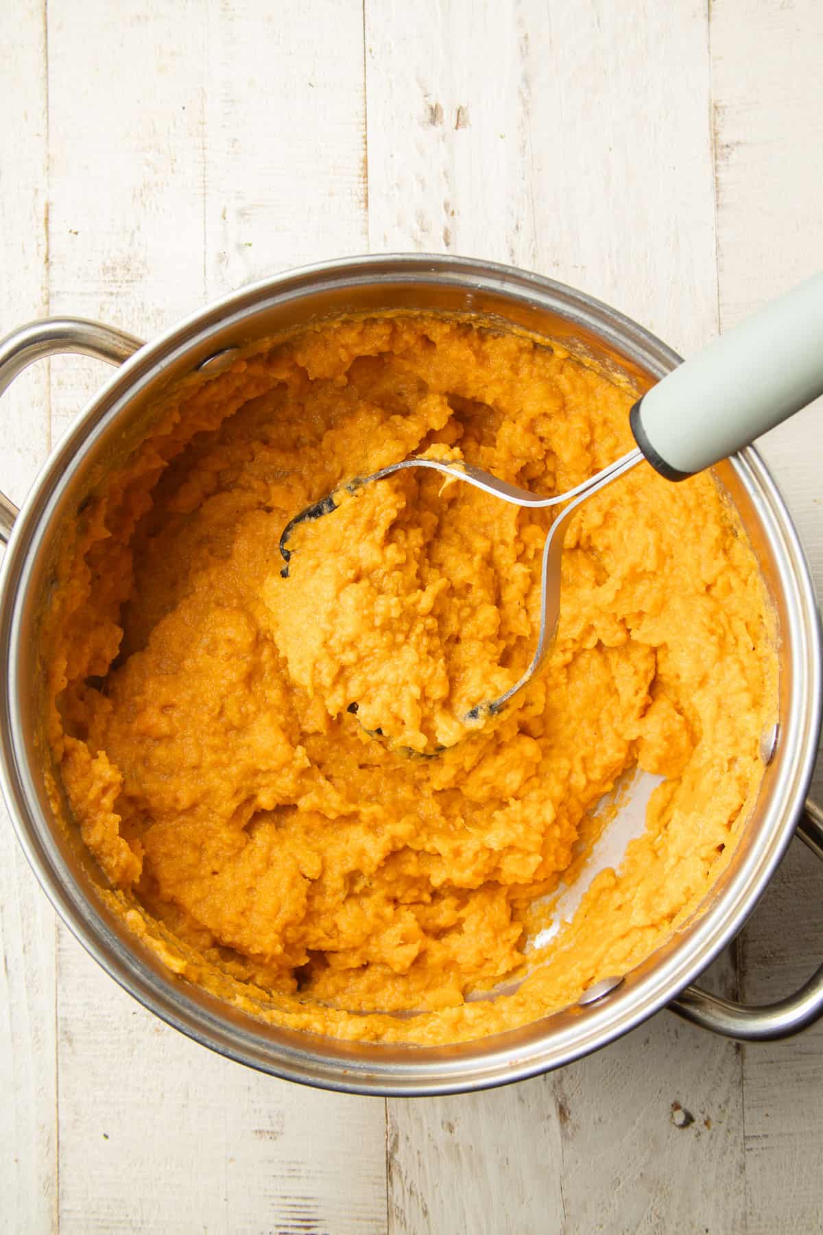 Vegan Mashed Sweet Potatoes in a pot with a potato masher.